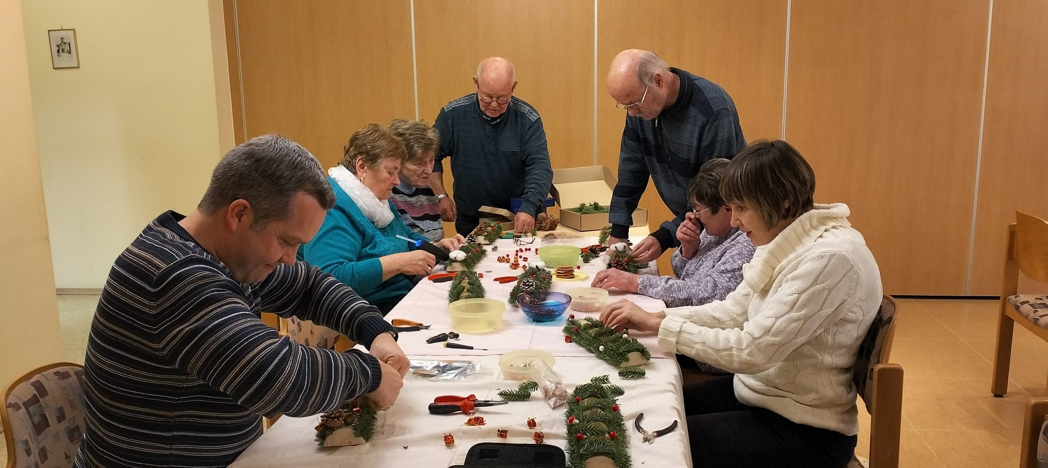 Mehrere Personen sitzen an einem Tisch und basteln gemeinsam mit verschiedenen Materialien Adventsleuchter.