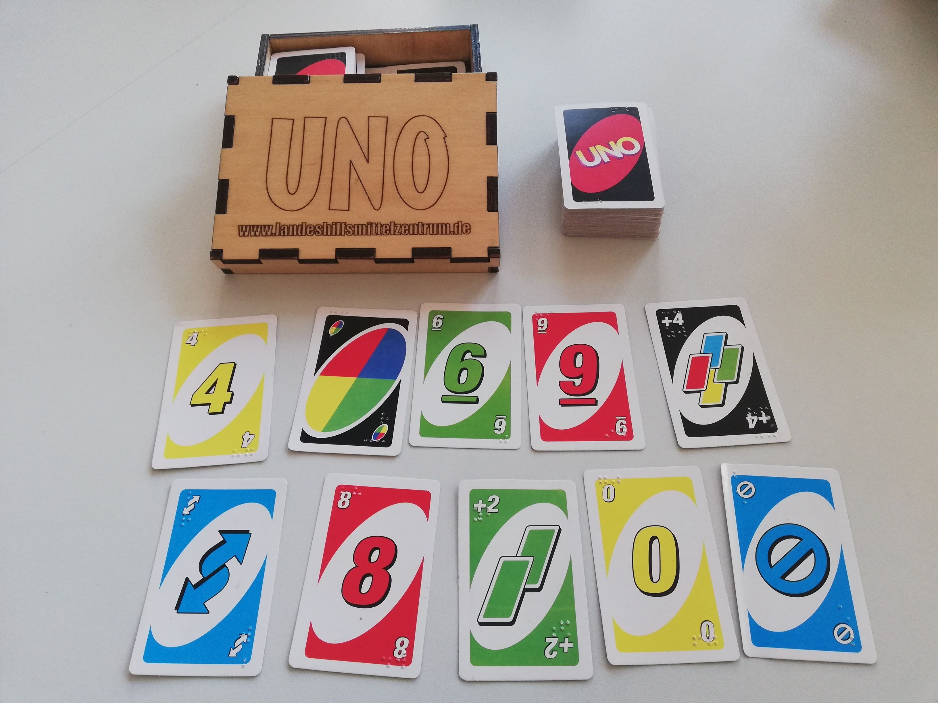 Kartenspiel mit großen Symbolen und Blindenschrift - zu sehen sind die Spieleschachtel und verschiedene Karten